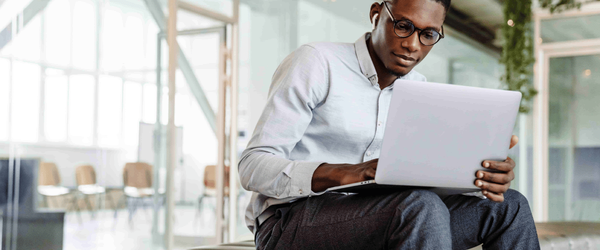Afro american young man in earphones working with laptop while sitting indoors